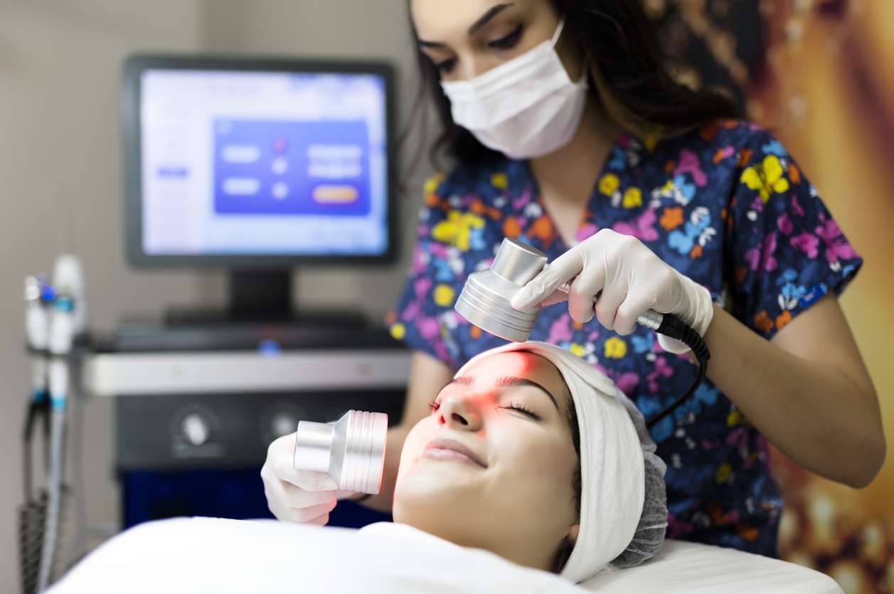 Cosmetologist making infrared light therapy facial treatment